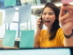 Excited woman organizing market research using sticky notes while talking on the phone, symbolizing the energy and enthusiasm in real estate market analysis.