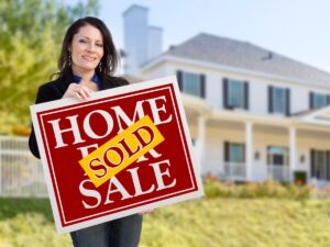 Real estate agent holding a "Sold" sign in front of a large home, symbolizing success in real estate transactions and the achievement of investment goals.