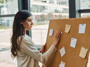 Woman entrepreneur organizing her thoughts and setting goals with a corkboard, symbolizing clarity and goal-setting in her professional journey.