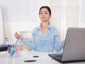 Woman entrepreneur taking a moment to meditate at her laptop, symbolizing mindfulness and stress management in a busy work environment.