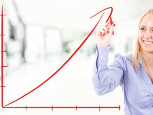 Smiling young woman drawing an upward-trending red line on a graph, symbolizing financial growth and business success.