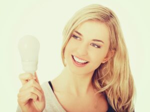 Smiling young woman holding a light bulb, symbolizing creativity and innovation.